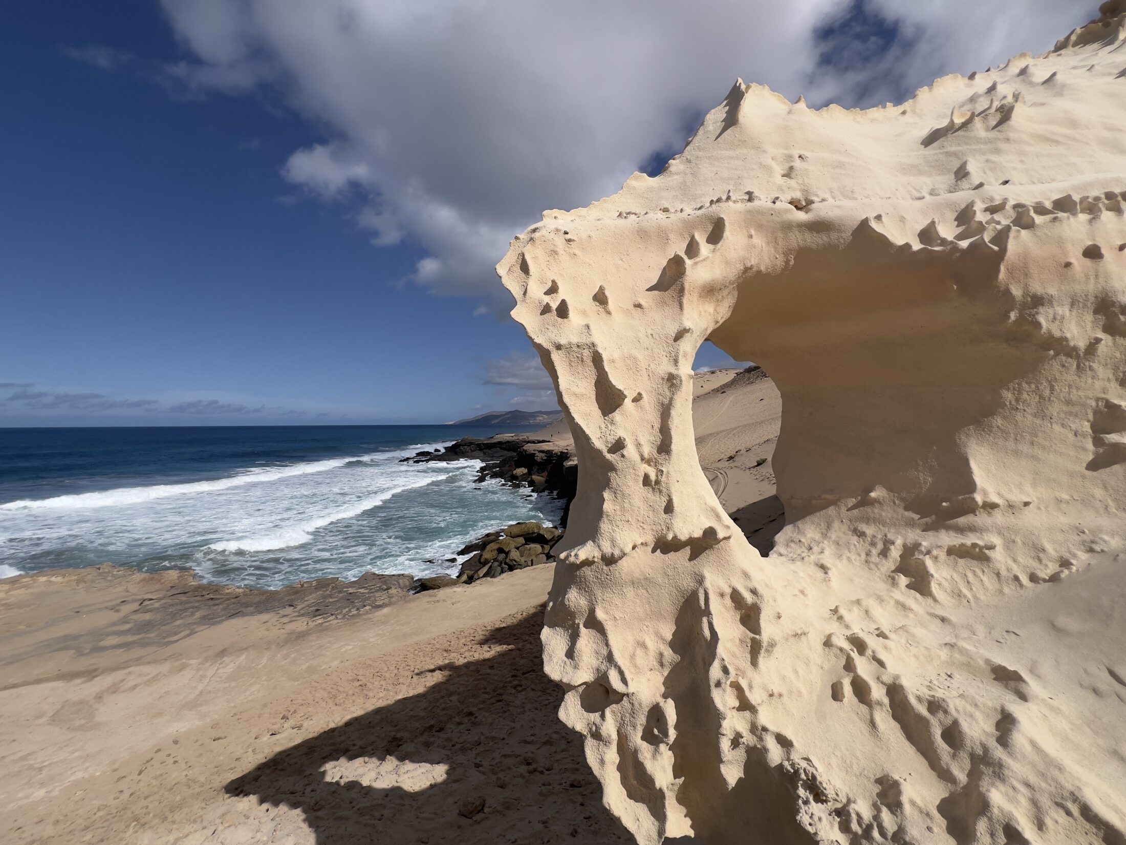 Meer und Küste im Hintergrund, im Vordergrund ein Sandstein mit einem Loch, durch das man sehen kann.