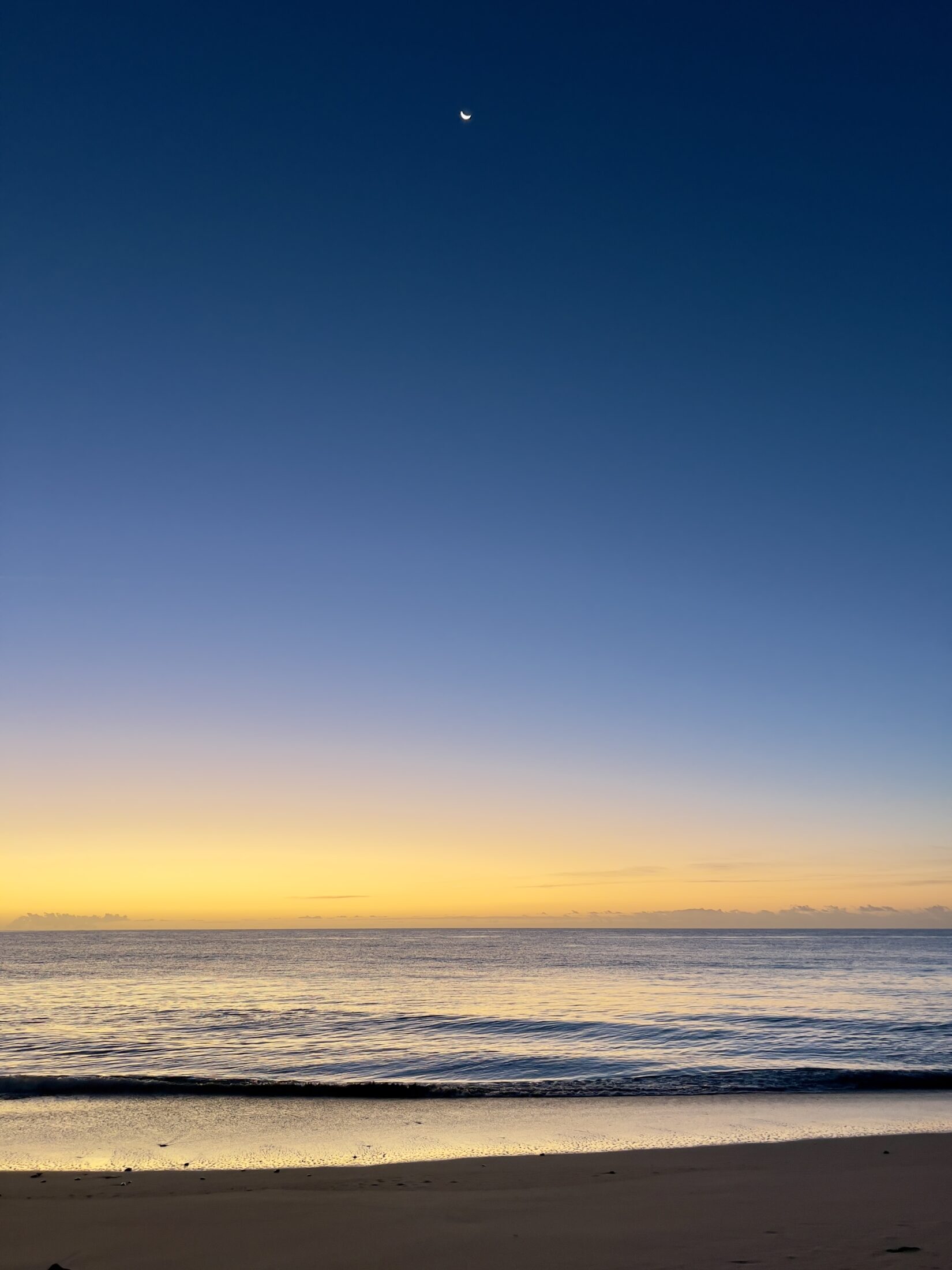 Meer mit Wellen und der Mond am Himmel. Der Horizont ist bereits orange kurz vor dem Sonnenaufgang