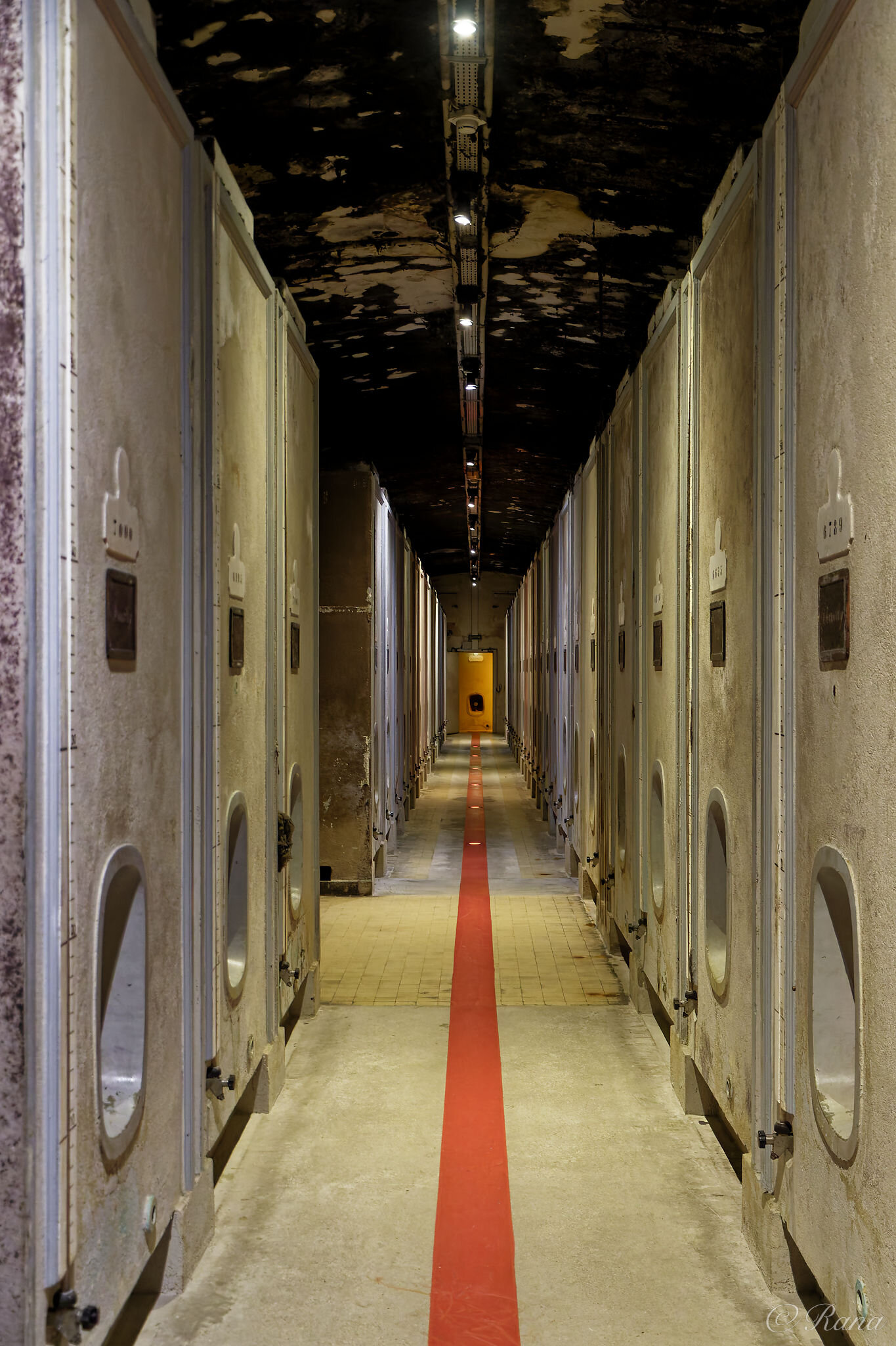 Links und rechts vom Gang stehen mehrere Betonfässer in Quaderform. Am Boden teilt ein roter Strich den Gang in zwei Hälften