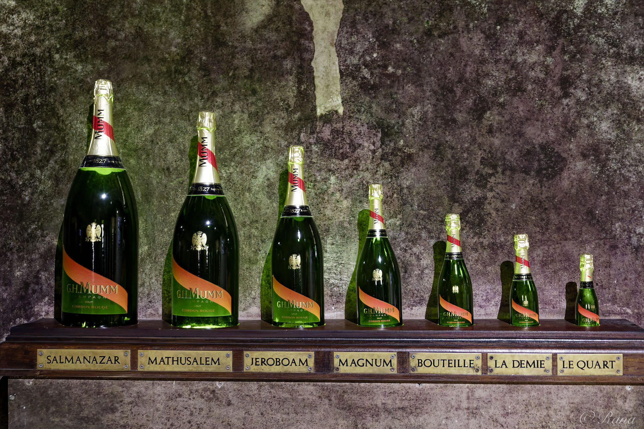 Unterschiedlich große Champagnerflaschen, von links nach rechts beschriftet mit: Salmanazar, Mathusalem, Jeroboam, Magnum, Bouteille, La Demie und Le Quart