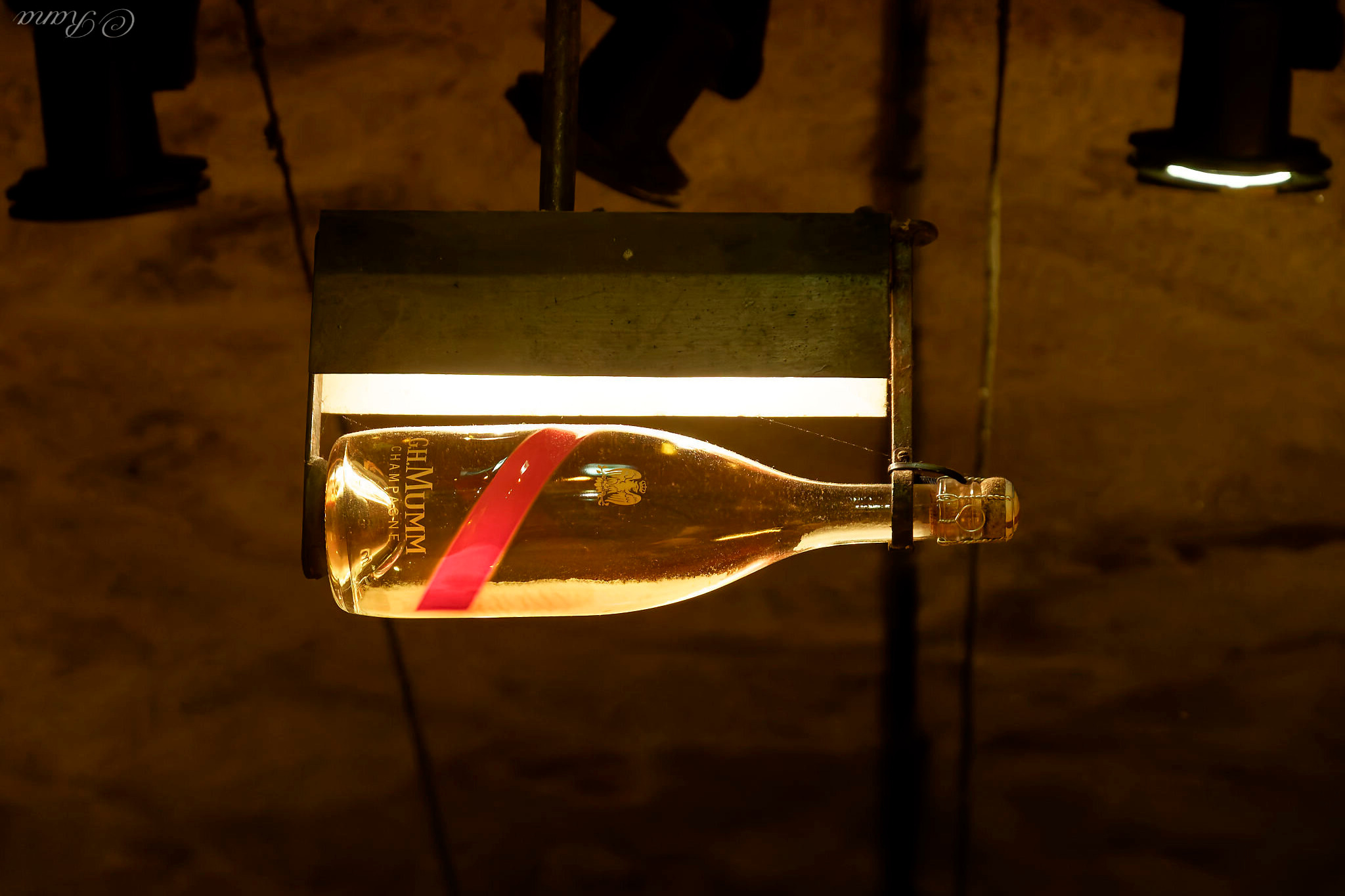 Eine beleuchtete waagerecht aufgehängte Champagnerflasche, auf der sich unten die Hefe sammelt