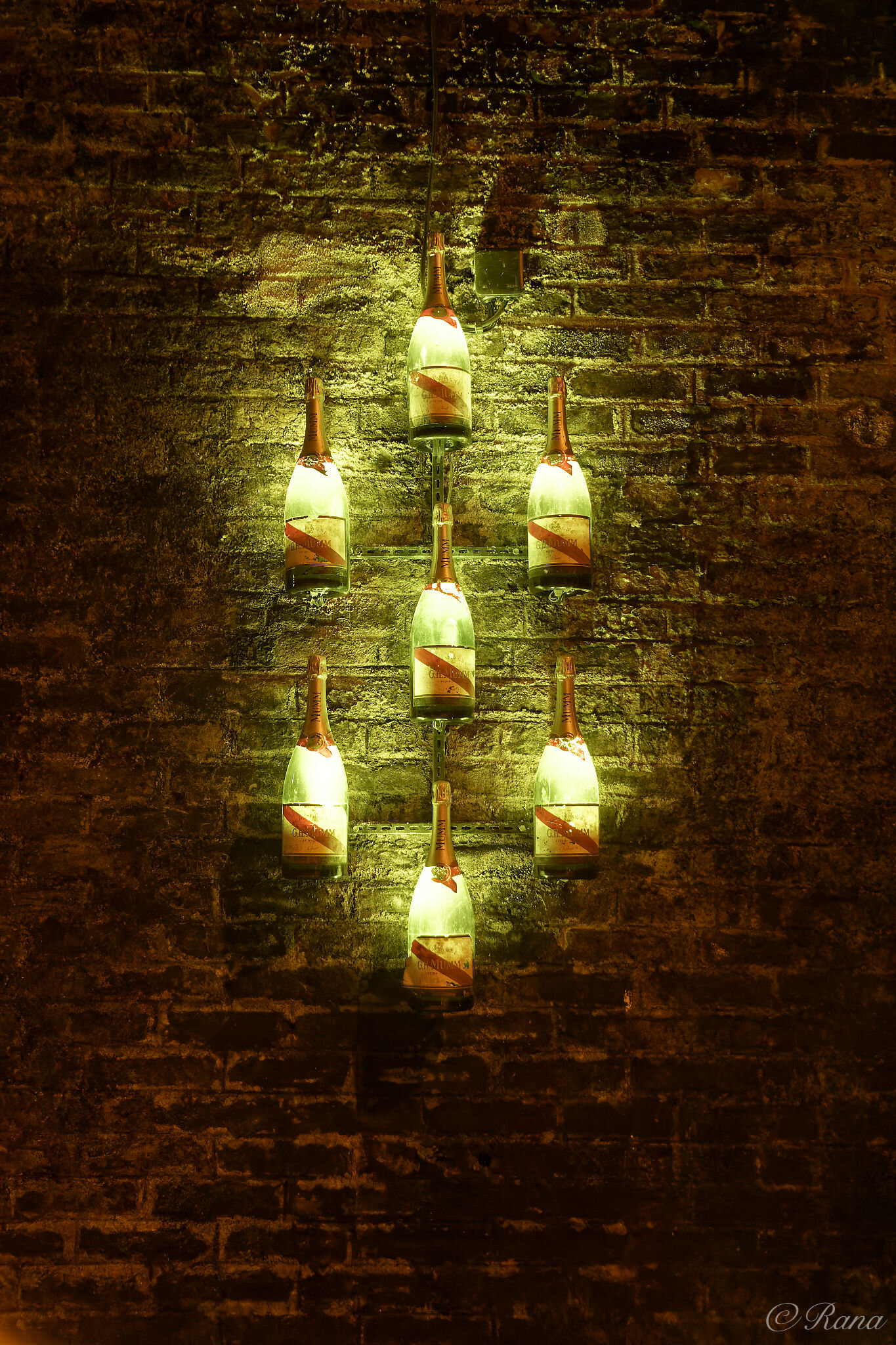 An einer Ziegelwand sind von innen beleuchtete Champagnerflaschen montiert