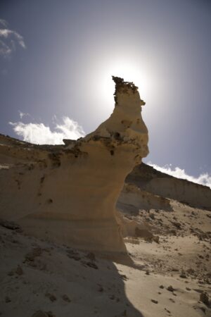 Ein Sandstein ragt schräg aus dem Sand. Die Spitze der Form verdeckt gerade die Sonne