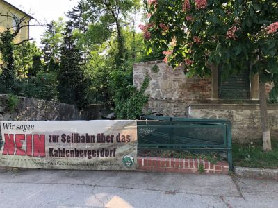 Transparent "Nein zur Seilbahn über das Kahlenbergerdorf" auf einem Gitter beim Waldbach im Kahlenbergerdorf