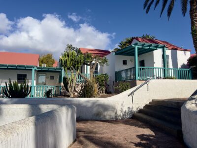Bungalows mit weißen Mauern und roten Dächern. Die Terrassen sind mit türkisen Holz eingefasst. Die Wege vor den Bungalows sind mit weißen hüfthauen Mauern eingefasst.