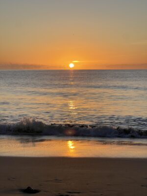 Die Sonne geht am Horizont über dem Meer auf. Eine Welle plätschert an den Sandstrand
